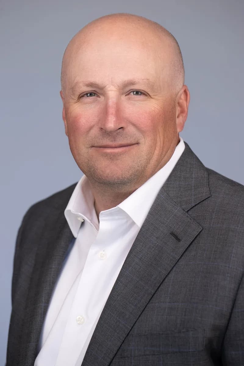 LinkedIn headshot of a man in a dark suit against a neutral backdrop