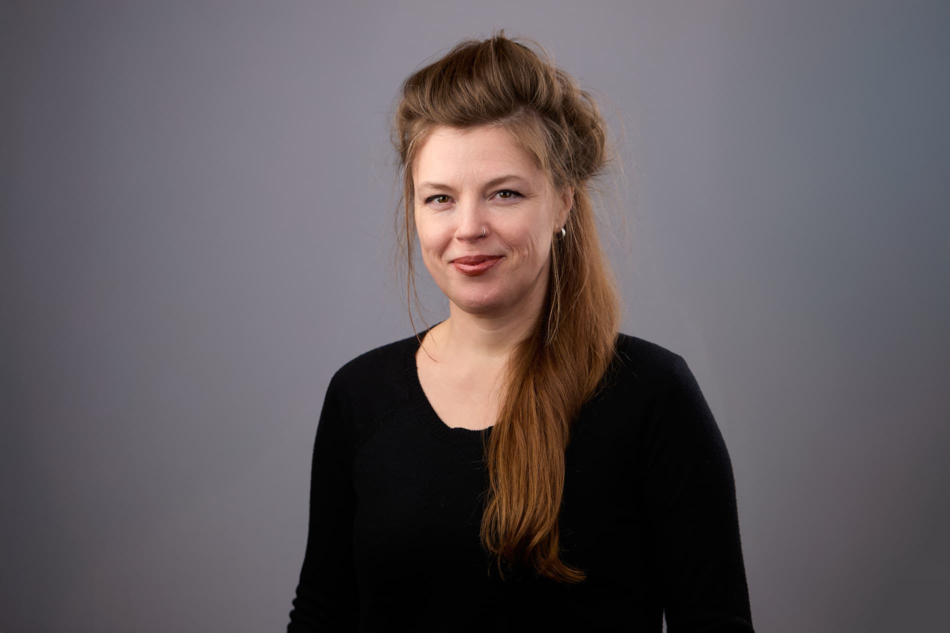 Professional headshot of woman with long reddish-brown hair in black top against gray background