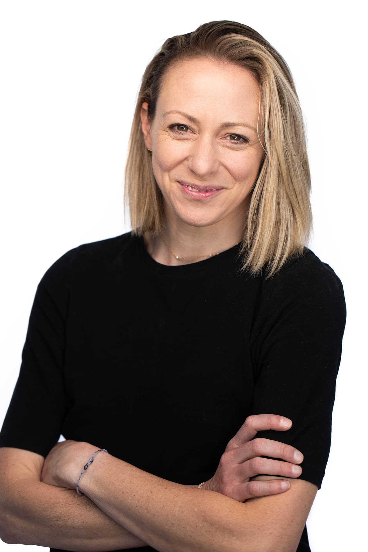 Professional headshot of a woman with shoulder-length blonde hair in a black top with arms crossed against a white background