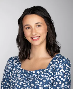 Professional headshot of a young woman with shoulder-length dark hair wearing a blue floral patterned top