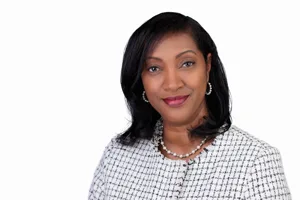 Professional headshot of a woman with black hair wearing a white and black patterned jacket and pearl necklace