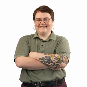 Professional headshot of a person with short brown hair and glasses wearing a green polo shirt with colorful tattoo
