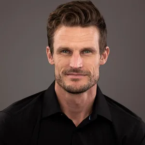 Professional headshot of a man with brown hair and beard wearing a black shirt against a dark background