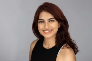 Professional headshot of a young woman with long reddish-brown hair wearing a black sleeveless top